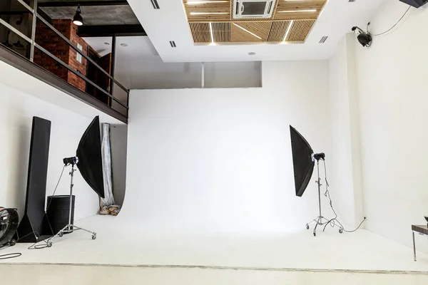 Empty photo studio with lighting equipment. Photographer workplace interior with professional tool set gear. Flash light, white background scenes ready for studio shooting. Modern photographer studio