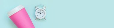 Düz dizayn edilmiş pembe kağıt kahve fincanı ve mavi pastel arka planda izole edilmiş çalar saat. Paket servis, kahvaltı içeceği. Günaydın uyanık kavramı. Üst görünüm kopyalama alanı afişi