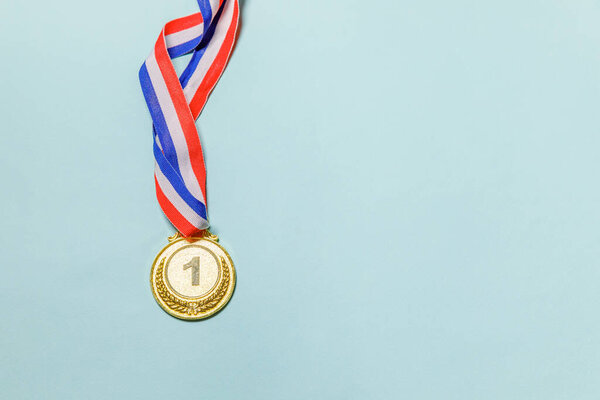 Simply flat lay design winner or champion gold trophy medal isolated on blue colorful background. Victory first place of competition. Winning or success concept. Top view copy space