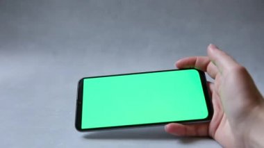 Cep telefonu tutan kadın, yeşil ekrana beton gri arka plandaki uygulamayı kullanarak dokunuyor. Yeşil krom anahtar ekranlı akıllı telefon modeli. İçeriğin yerleştirilmesi için boş ekran krom anahtarı.