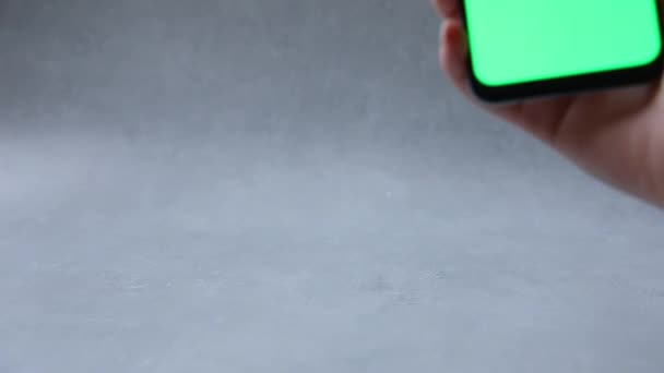 Mujer sosteniendo la mano teléfono celular táctil pantalla verde utilizando aplicación sobre fondo gris piedra de hormigón. Smartphone maqueta con pantalla de clave de croma verde. Tecla de croma de pantalla en blanco para la colocación de contenido. — Vídeo de stock