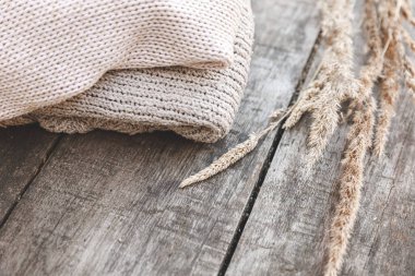Sonbahar ya da kış geçmişi. Bir yığın yün kazak ve ahşap masada kurutulmuş bitki. Hygge havası, soğuk hava konsepti. El yapımı örgü kazaklar.