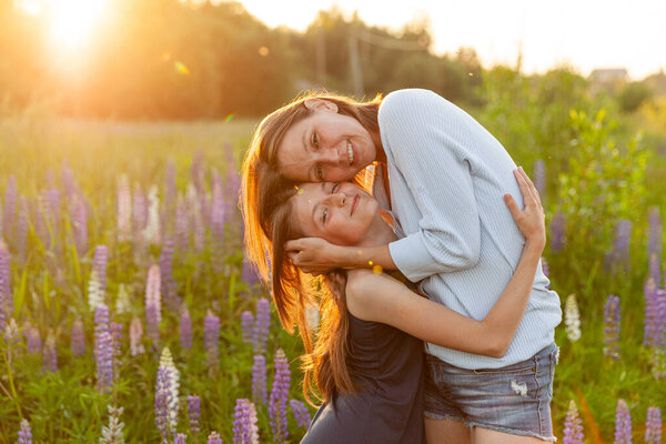 Young mother embracing her child outdoor. Woman and teenage girl on summer field with blooming wild flowers green background. Happy family mom and daughter playing on meadow