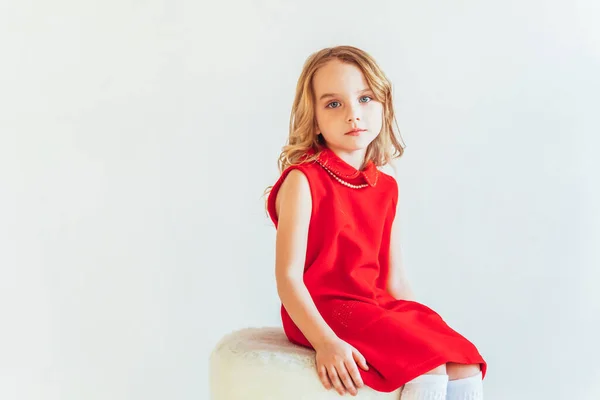 白い明るいリビングルームに屋内でリラックスし 自宅で白い壁に対して椅子に座って赤いドレスの甘い女の子 子供の頃の若者のリラックスコンセプト — ストック写真