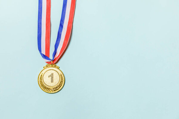 Simply flat lay design winner or champion gold trophy medal isolated on blue colorful background. Victory first place of competition. Winning or success concept. Top view copy space