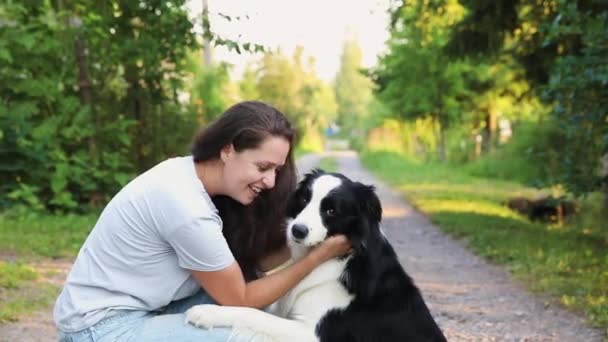 Smiling young attractive woman playing with cute puppy dog border collie on summer outdoor background. Girl holding embracing hugging dog friend. Pet care and animals concept. — Stock Video