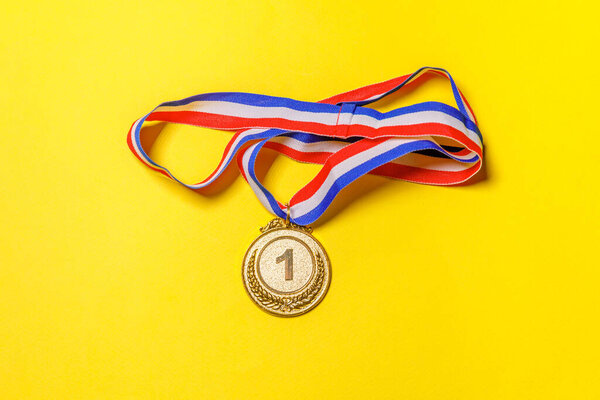 Simply flat lay design winner or champion gold trophy medal isolated on yellow colorful background. Victory first place of competition. Winning or success concept. Top view copy space.