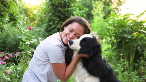 Smiling young attractive woman playing with cute puppy dog border collie on summer outdoor background. Girl holding embracing hugging dog friend. Pet care and animals concept. — Stock Video