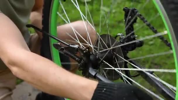 Mecánico de bicicletas reparaciones hombre bicicleta en taller de reparación de bicicletas, al aire libre. Mano de ciclista ciclista examina, fija el sistema de transmisión de ciclo moderno. Mantenimiento de bicicletas, concepto de tienda de deporte. — Vídeo de stock