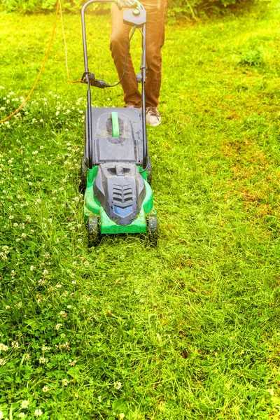 Человек стрижет зеленую траву газонокосилкой на заднем дворе. Садоводство деревенский образ жизни. Прекрасный вид на лужайку из свежей зеленой травы на солнце, пейзаж сада весной или летом. — стоковое фото