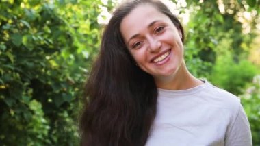 Dışarıda gülümseyen genç bir kadın. Güzel esmer kız parkta dinleniyor ya da bahçe yeşili arka planda. Yazın özgür ve mutlu bir kadın. Özgürlük mutluluğu tasasız mutlu insanlar konsepti.