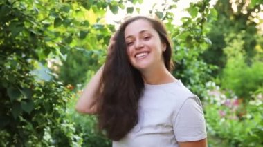 Dışarıda gülümseyen genç bir kadın. Güzel esmer kız parkta dinleniyor ya da bahçe yeşili arka planda. Yazın özgür ve mutlu bir kadın. Özgürlük mutluluğu tasasız mutlu insanlar konsepti.