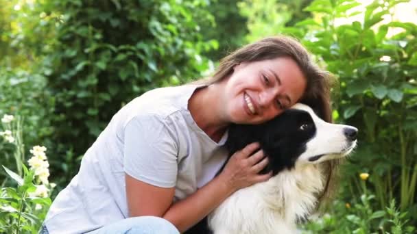 Lächelnde junge attraktive Frau, die mit niedlichen Hundewelpen Border Collie auf sommerlichem Outdoor-Hintergrund spielt. Mädchen umarmt umarmende Hundefreundin. Haustierpflege und Tierkonzept. — Stockvideo