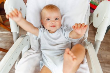 Beyaz arka planda kameraya bakan gülümseyen yeni doğmuş şirin bir kız. Bebek dinleniyor ve evdeki beslenme sandalyesine uzanıyor. Annelik mutlu çocuk konsepti.