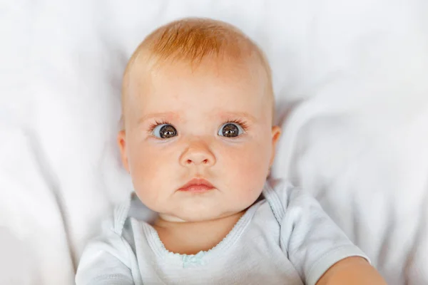 Linda niña recién nacida con cara divertida mirando a la cámara en el fondo blanco. Bebé descansando jugando acostado en la cama de la cuna en casa. Maternidad niño feliz concepto. —  Fotos de Stock