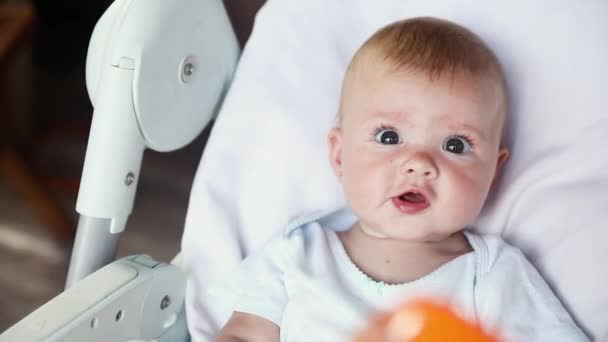 Χαριτωμένο μικρό νεογέννητο κορίτσι με χαμογελαστό πρόσωπο κοιτάζοντας κάμερα σε λευκό φόντο. Βρέφος μωρό αναπαύεται παίζοντας ξαπλωμένος σε καρέκλα σίτισης στο σπίτι. Μητρότητα ευτυχισμένη έννοια του παιδιού. — Αρχείο Βίντεο