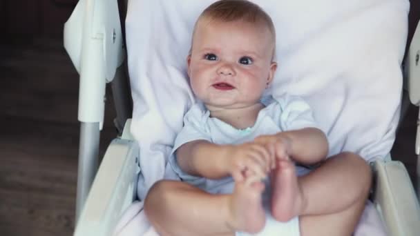 Menina recém-nascido bonito com rosto sorridente olhando para a câmera no fundo branco. Bebê infantil descansando brincando deitado na cadeira de alimentação em casa. Conceito de criança feliz maternidade. — Vídeo de Stock