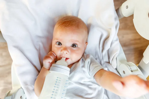 젖병에서 우유를 마시고 하얀 배경에 카메라를 보고 있는 귀여운 신생아. 가정에서 급식 의자에 누운 우유 영양을 빨아먹는 젖먹이 아기. 행복 한 어머니의 자녀 — 스톡 사진