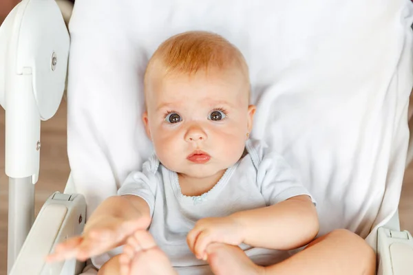 Drăguță fetiță nou-născută cu față zâmbitoare uitându-se la camera de pe fundal alb. Bebelușul se odihnește jucându-se pe scaunul de hrănire acasă. Conceptul de copil fericit pentru maternitate . — Fotografie, imagine de stoc