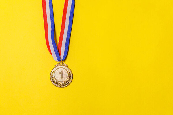 Simply flat lay design winner or champion gold trophy medal isolated on yellow colorful background. Victory first place of competition. Winning or success concept. Top view copy space