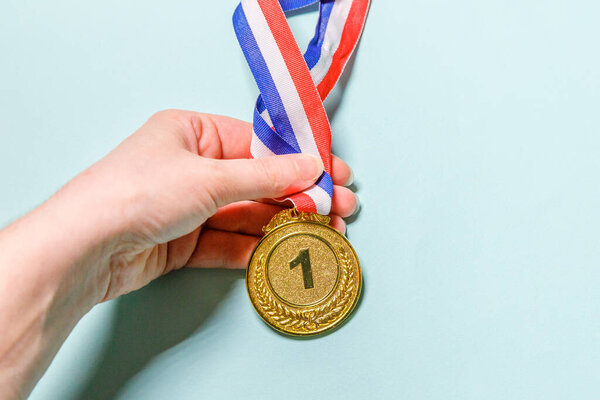 Simply flat lay design hand holding winner or champion gold trophy medal isolated on blue colorful background. Victory first place of competition. Winning or success concept. Top view copy space