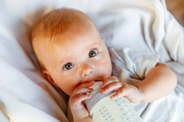 젖병에서 우유를 마시고 배경에 카메라를 귀여운 신생아 아기는 침대에 젖먹이의 — 스톡 사진