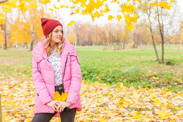 Happy young woman playing with falling yellow leaves in beautiful autumn park on nature walks outdoors. Teenage girl holding autumn orange maple leaf