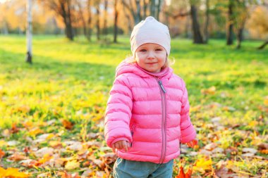 Güzel sonbahar parkında, doğa yürüyüşlerinde gülümseyen mutlu genç kız. Sonbaharda oynayan küçük çocuk turuncu arka planda sonbaharda oynuyor. Merhaba sonbahar konsepti