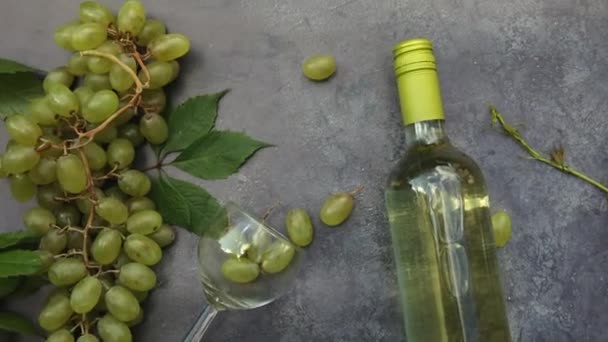 Draufsicht auf Flasche Weißwein, grüne Rebe, Weinglas und reife Trauben auf dunklem Steintischhintergrund. Vinothek Weinbar Weingut oder Weinverkostungskonzept. — Stockvideo