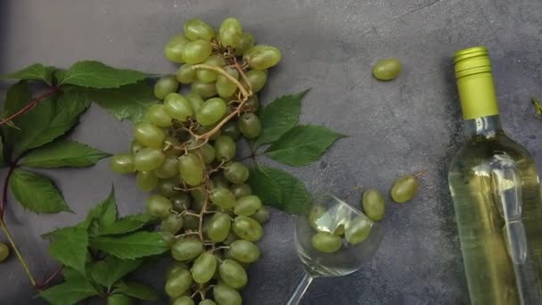 Horní pohled na láhev bílého vína, zelené vinné révy, vinné sklo a zralé hrozny na vinobraní tmavé kamenné pozadí stolu. Vinotéka vinařství nebo víno degustační koncept. — Stock video