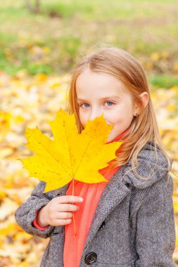 Sarı yapraklarla oynayan mutlu genç bir kız güzel bir sonbahar parkında doğa yürüyüşünde. Sonbahar portakal yaprağı tutan küçük çocuk.