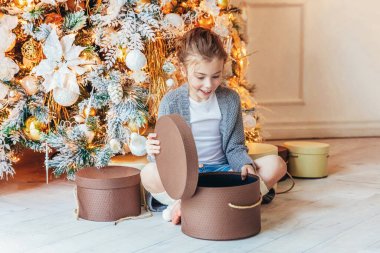 Noel arifesinde Noel ağacının yanında hediye kutusu olan küçük bir kız. Küçük çocuk kış dekorasyonlu, açık renk yatak odasında. Noel Yeni Yıl Kutlama Konsepti Zamanı