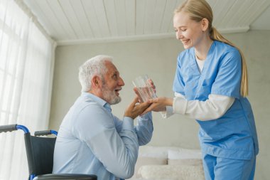 Sağlık hizmetleri su dengesini desteklemeye yardımcı olur. Hemşire tekerlekli sandalyedeki yaşlı adam için cam su veriyor. Engelliler için tekerlekli sandalyedeki felçli adam taze su içiyor. Kıdemli adam ve hemşire evde.