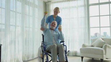 Rehabilitasyon sağlık hizmetlerini destekleyin. Hemşire, tekerlekli sandalyedeki yaşlı hastaya dambılları toplamasında yardım ediyor. Engelli insanlar için tekerlekli sandalyede oturan sakat bir adam hemşireyle spor egzersizi yapıyor. Tıbbi bakıcı.
