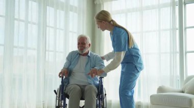 Rehabilitasyon sağlık hizmetleri. Fizyoterapist hemşire tekerlekli sandalyedeki yaşlı adamın ayağa kalkmasına yardım ediyor. Engelli insanlar için sandalyedeki adam hemşire yardımı ile birkaç adım atıyor. Tıbbi bakıcı.