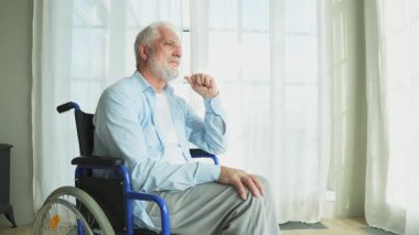 Tekerlekli sandalyede oturan üzgün yaşlı adam huzurevinin penceresinden dışarı bakıyor. Engelli insanlar için tekerlekli sandalyedeki yaşlı felçli adam depresyonda. Yalnız yaşlı hasta adam tekerlekli sandalyede oturuyor.