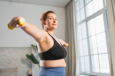 Fitness antrenmanı. Dambılları kaldıran kadın. Artı ev içinde spor egzersizi yapan beden bir kadın. Spor giyimli kız kilo vermek için ağırlık çalışması yapıyor. Spor ve zindelik