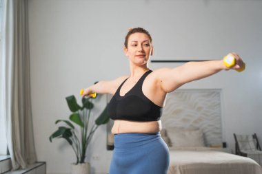 Fitness antrenmanı. Dambılları kaldıran kadın. Artı ev içinde spor egzersizi yapan beden bir kadın. Spor giyimli kız kilo vermek için ağırlık çalışması yapıyor. Spor ve zindelik