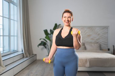 Fitness antrenmanı. Dambılları kaldıran kadın. Artı ev içinde spor egzersizi yapan beden bir kadın. Spor giyimli kız kilo vermek için ağırlık çalışması yapıyor. Spor ve zindelik