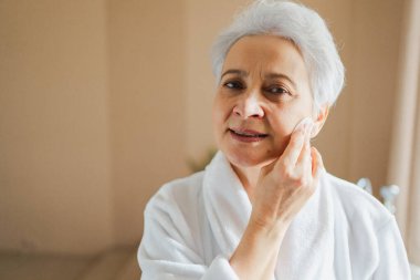 Yetişkin, yaşlı bir kadın günlük güzellik rutini yapıyor pamukla makyaj yapıyor. Losyon süngerli yaşlı kadın yüz bakımı yaptırıyor. Cilt bakımı yaşlandırıcı cilt temizleyici