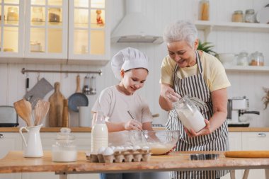 Mutfakta mutlu bir aile. Büyükannem ve torunum mutfakta birlikte yemek pişiriyorlar. Küçük kıza hamur yoğurmayı öğreten büyükanne kurabiye pişiriyor. Ev işi aile oluşturma kavramına yardımcı oluyor