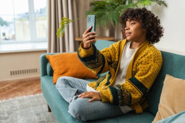 African American girl holding smartphone having video chat. Female blogger chatting with best friends in social network. Young woman having virtual meeting online chat video call at home