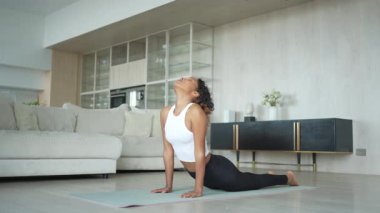 Yoga fitness antrenmanı. Sağlıklı Afrikalı kız evde yoga yapıyor. Pilates antrenmanı yapan bir kadın, yoga minderiyle spor yapıyor. Kız kilo vermek için antrenman yapıyor. Spor uygunluğu