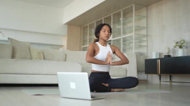 Yoga farkındalığı meditasyonu çevrimiçi. Afrikalı kadın evdeki bilgisayarında online derslerle yoga yapıyor. Lotus 'ta oturan kadın meditasyon yapıyor. Nefes egzersizi yapan bir kız. Evde yoga.