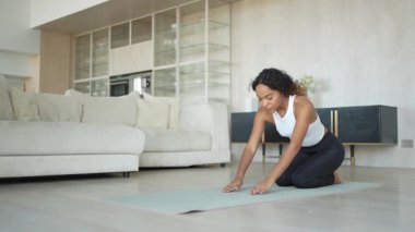 Yoga fitness antrenmanı. Sağlıklı Afrikalı kız evde yoga yapıyor. Pilates antrenmanı yapan bir kadın, yoga minderiyle spor yapıyor. Kız kilo vermek için antrenman yapıyor. Spor uygunluğu