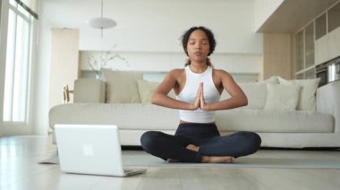 Yoga farkındalığı meditasyonu çevrimiçi. Afrikalı kadın evdeki bilgisayarında online derslerle yoga yapıyor. Lotus 'ta oturan kadın meditasyon yapıyor. Nefes egzersizi yapan bir kız. Evde yoga.