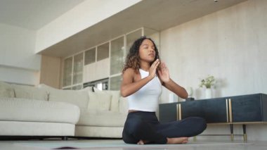 Yoga farkındalığı meditasyonu. Genç sağlıklı Afrikalı kız evde yoga yapıyor. Lotus 'ta oturan kadın yoga minderinde poz veriyor içeride meditasyon yapıyor. Nefes egzersizi yapan bir kız. Evde yoga.