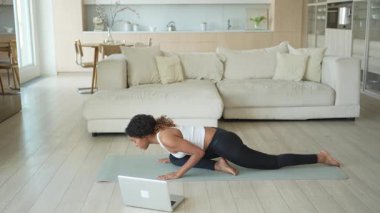 Yoga fitness antrenmanı online. Afrikalı kadın evdeki bilgisayarında online derslerle yoga yapıyor. Yoga minderinde spor yapan bir kız. Kadın kilo vermek için egzersiz yapıyor. Spor uygunluğu