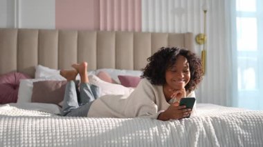 African girl holding smartphone touch screen typing scroll page at home. Woman with cell phone surfing internet using social media apps playing game. Shopping online Internet news cellphone addiction