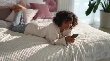 African girl holding smartphone touch screen typing scroll page at home. Woman with cell phone surfing internet using social media apps playing game. Shopping online Internet news cellphone addiction